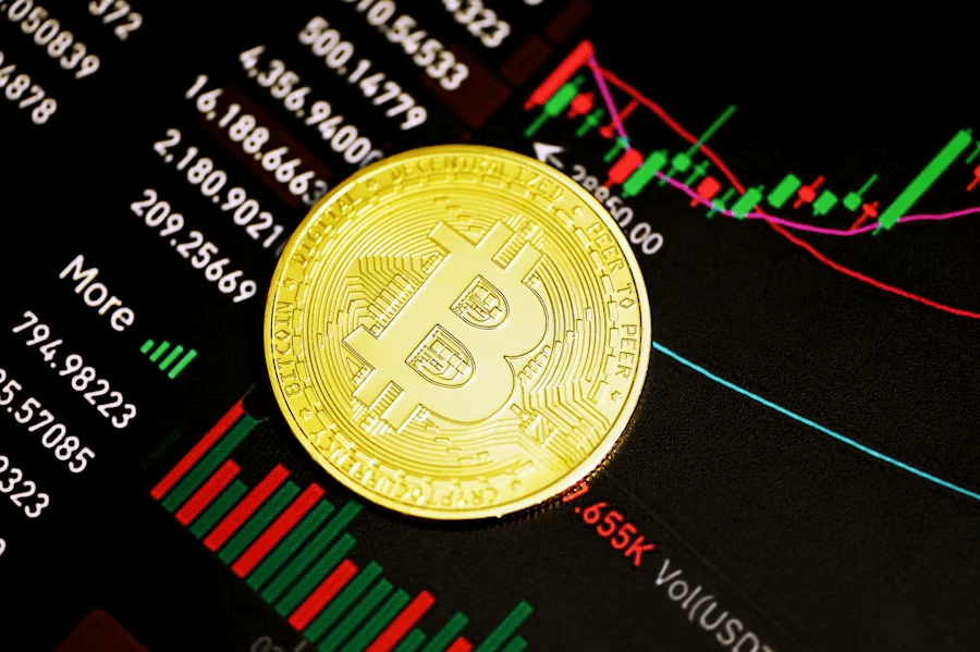 Złota moneta Bitcoin leżąca na ekranie z wykresami cen i danymi handlowymi w kolorze zielonym i czerwonym