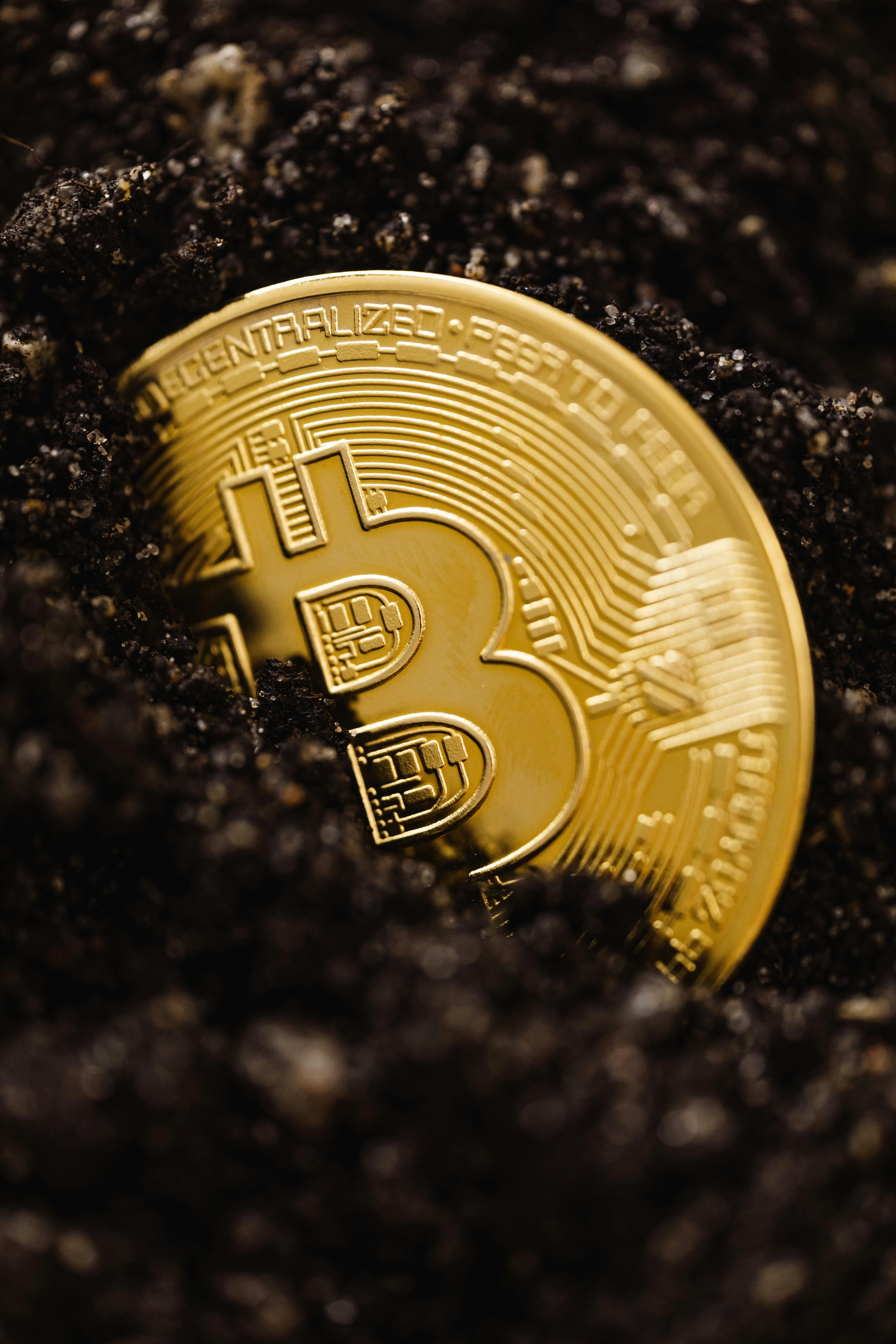 Złota moneta Bitcoin do połowy zakopana w ciemnej ziemi, symbol ukrytej wartości i długoterminowej inwestycji krypto.